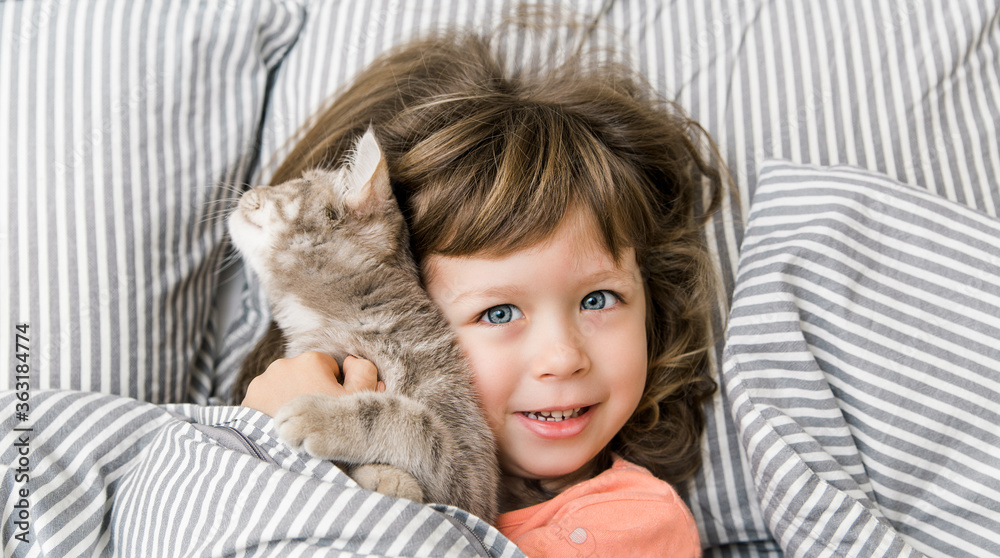 Portrait of child girl with her pet in bed. Little girl smilling and having fun in bed. Funny quarantine house isolation. COVID 19 Portrait of child girl with her pet in bed. Little girl smilling and having fun in bed. Funny quarantine house isolation. COVID 19