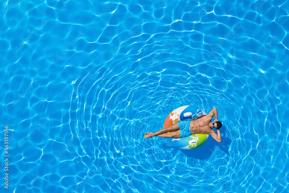 Young man with inflatable ring in swimming pool, top view. Space for text