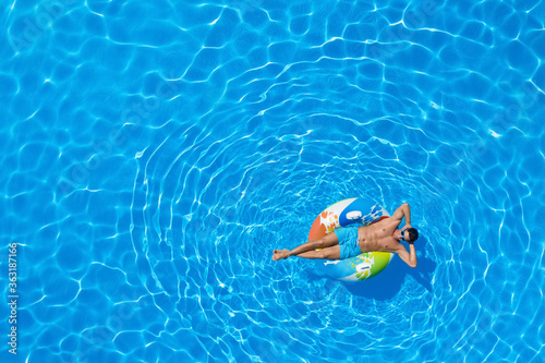 Young man with inflatable ring in swimming pool, top view. Space for text