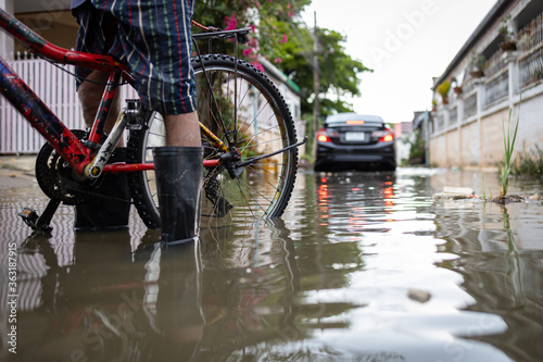 Person wear rubber boots,prevent infection of leptospirosis,athlete's foot,disease from dirty water,male in waterproof boots in a puddle on a flooded street,car is driving through floods in background
