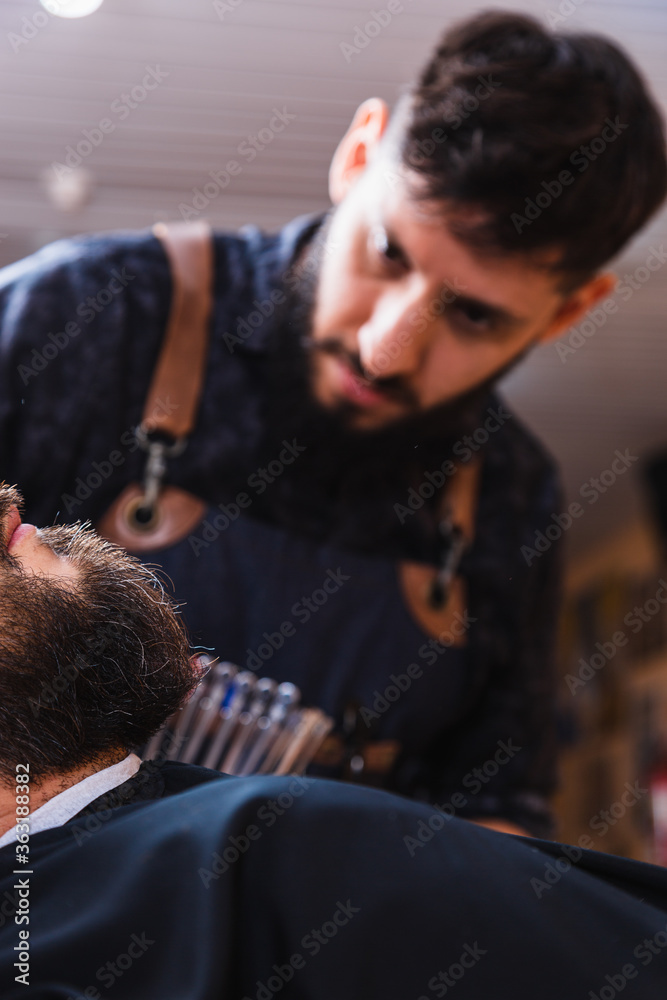 Barber focused on fixing his client's beard. The focus is on the client's beard. Barber focused on fixing his client's beard. The focus is on the client's beard.