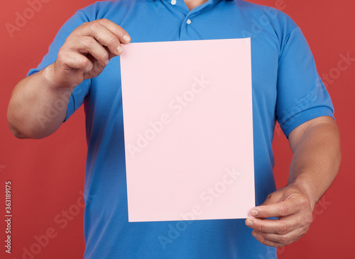 man in blue clothes holds an empty sheet of pink paper on a red background