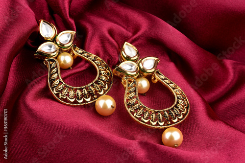 Beautiful Golden pair of earrings Diamonds gemstones on a red satin background. Luxury female jewelry, Indian traditional jewellery, kundan earring,Bridal Gold earrings wedding jewellery