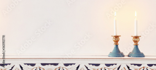 two shabbat candlesticks with burning candles over wooden table photo