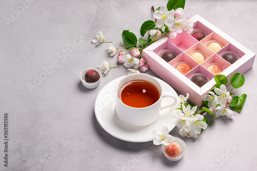 Chocolates of various colors in a festive elegant box packing a cup of tea on pastel pink background decoration flowers.