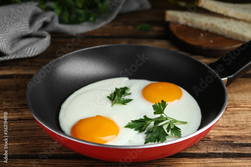 Tasty cooked chicken eggs with parsley in frying pan on wooden table, closeup