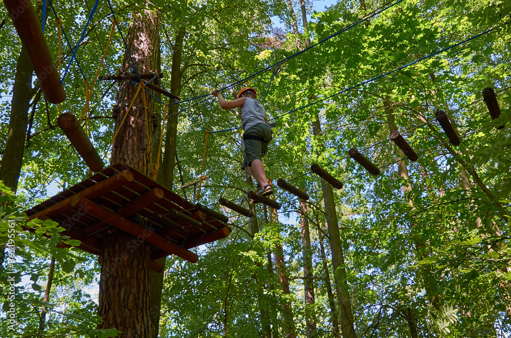 Fototapeta premium A boy with a helmet and insurance passes a high-altitude obstacle course.