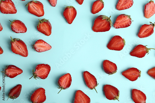 Halves of delicious ripe strawberries on light blue background, flat lay