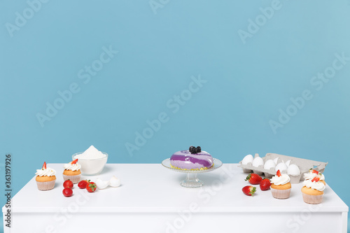 Confectioner baker chef white table with ingredients for cooking cake or cupcake eggs strawberry flour isolated on blue wall background in studio. Mock up copy space food concept. Nobody interior. © ViDi Studio