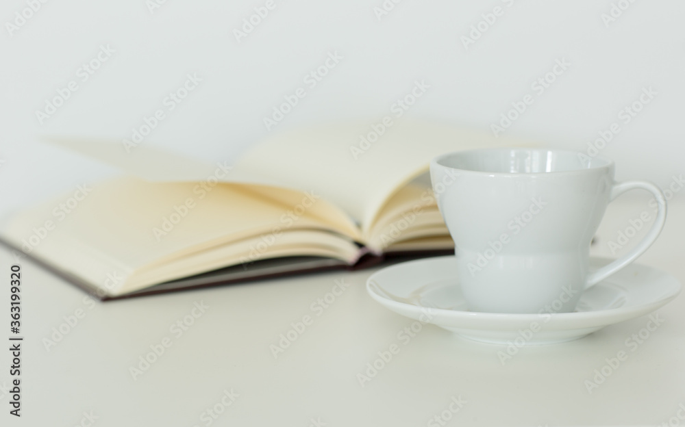 Open notebook with blank pages lying flat next to a coffee cup on a saucer. Isolated against white background. Calm study and relaxation. Open notebook with blank pages lying flat next to a coffee cup on a saucer. Isolated against white background. Calm study and relaxation.