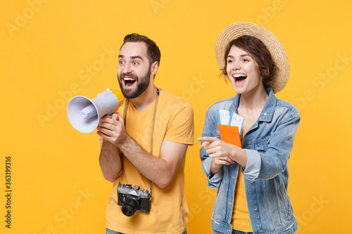 Excited young tourists couple friends guy girl isolated on yellow background. Passenger traveling abroad on weekends. Air flight journey concept. Hold passport tickets megaphone pointing finger aside.