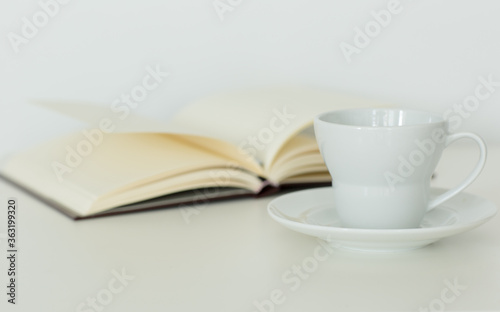 Open notebook with blank pages lying flat next to a coffee cup on a saucer. Isolated against white background. Calm study and relaxation. 