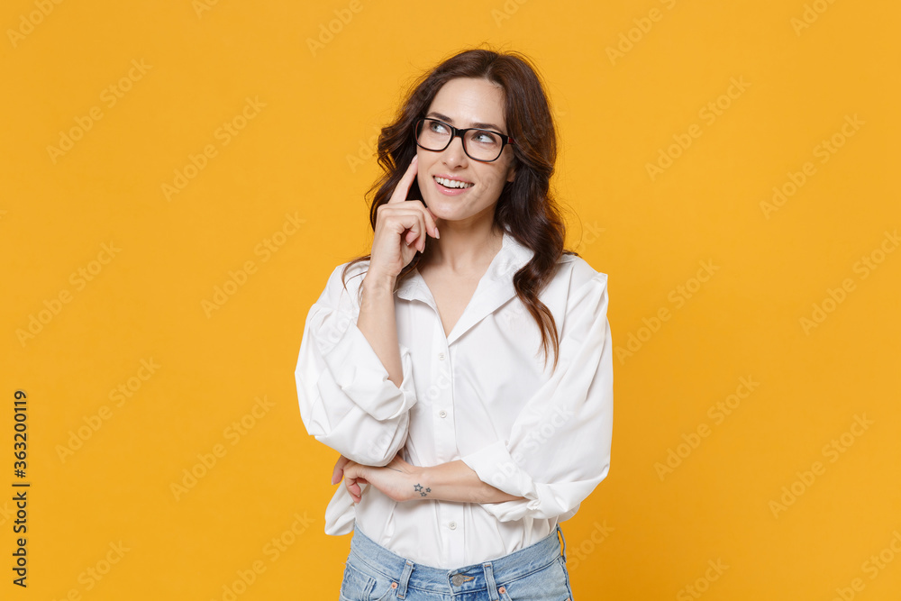 Pensive young brunette business woman in white shirt glasses isolated on yellow background studio. Achievement career wealth business concept. Mock up copy space. Put hand prop up on chin, looking up. Pensive young brunette business woman in white shirt glasses isolated on yellow background studio. Achievement career wealth business concept. Mock up copy space. Put hand prop up on chin, looking up.