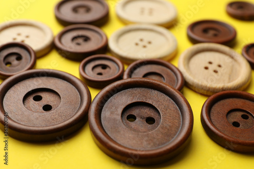 Many colorful sewing buttons on yellow background, closeup