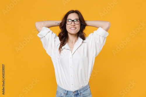 Pensive young business woman in white shirt glasses isolated on yellow background studio portrait. Achievement career wealth business concept. Mock up copy space. Looking up with hands behind head.