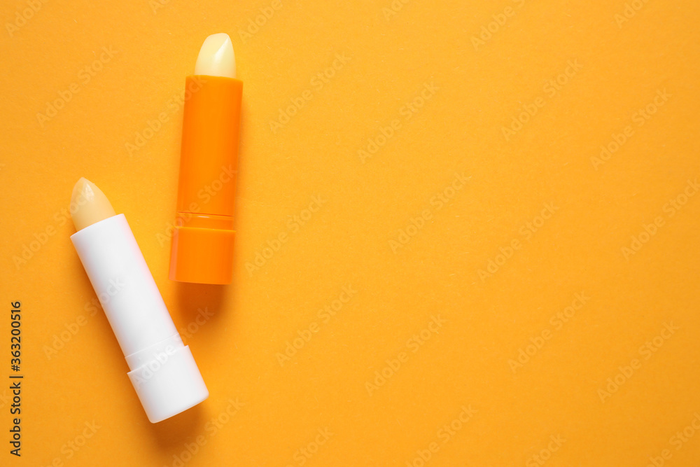 Hygienic lipsticks on orange background, flat lay. Space for text