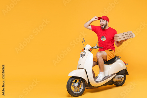 Delivery man in red cap t-shirt uniform driving moped motorbike scooter hold pizza in cardboard flatbox isolated on yellow background studio Fun guy employee working courier Service quarantine concept © ViDi Studio