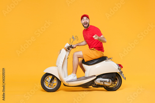 Delivery man in red cap t-shirt uniform driving moped motorbike scooter isolated on yellow background studio Guy employee working courier Service quarantine pandemic coronavirus virus covid-19 concept