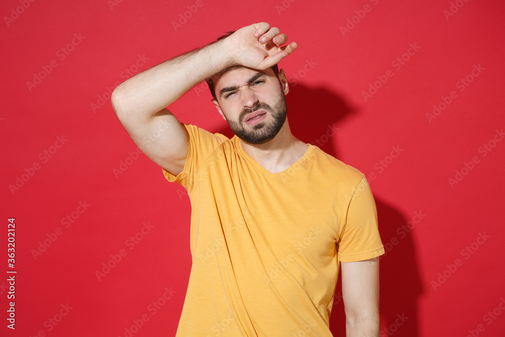 Exhausted tired young bearded man guy in casual yellow t-shirt posing isolated on red wall background studio portrait. People sincere emotions lifestyle concept. Mock up copy space. Put hand on head. Exhausted tired young bearded man guy in casual yellow t-shirt posing isolated on red wall background studio portrait. People sincere emotions lifestyle concept. Mock up copy space. Put hand on head.