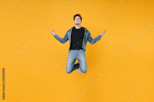 Relaxed young man guy 20s wearing casual denim clothes posing isolated on yellow wall background. People lifestyle concept. Mock up copy space. Jumping hold hands in yoga gesture, relaxing meditating.