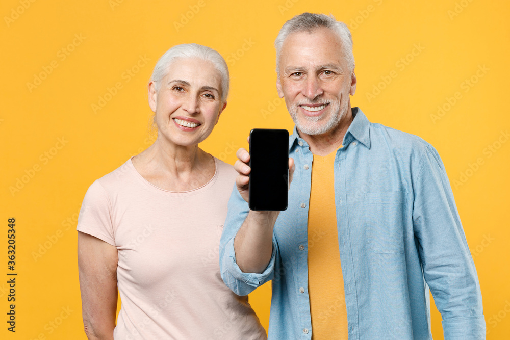 Smiling elderly gray-haired couple woman man in casual clothes isolated on yellow background studio portrait. People lifestyle concept. Mock up copy space. Hold mobile phone with blank empty screen. Smiling elderly gray-haired couple woman man in casual clothes isolated on yellow background studio portrait. People lifestyle concept. Mock up copy space. Hold mobile phone with blank empty screen.