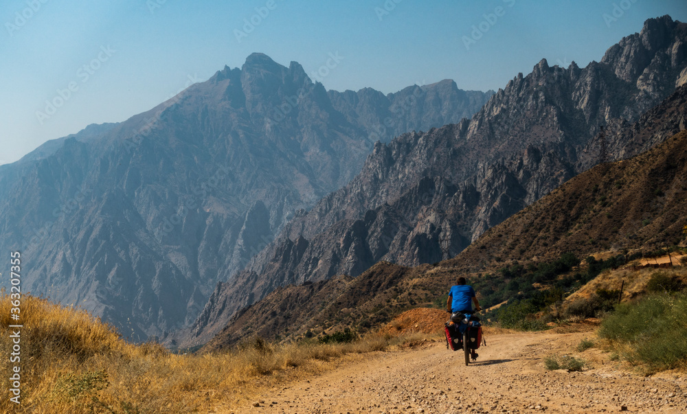 Cycle traveler on a dirt road with large mountains in the background