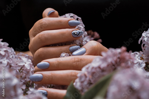 Beautiful female nails with lilac, art manicure and lilac flowers on a black background photo