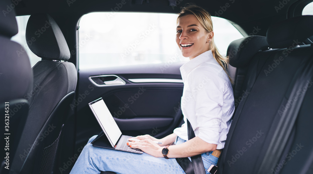 Portrait of happy hipster girl in casual apparel looking at camera and smiling while using 4g wireless internet connection for networking via modern touch pad during car trip to destination
