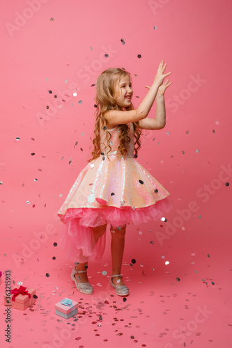 happy Little girl catches confetti on pink background, holiday concept