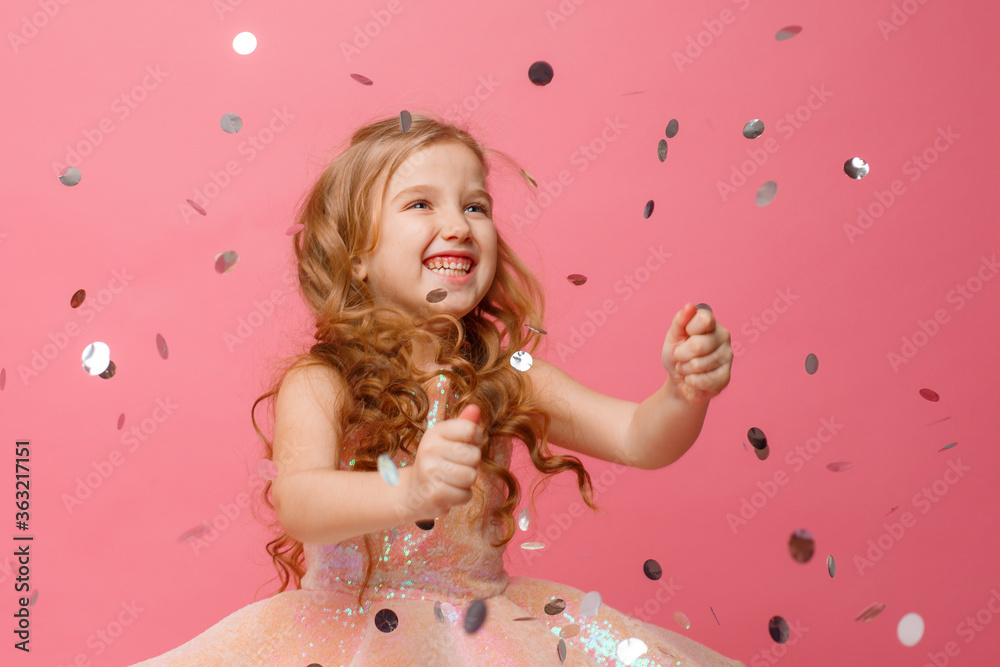 happy Little girl catches confetti on pink background, holiday concept