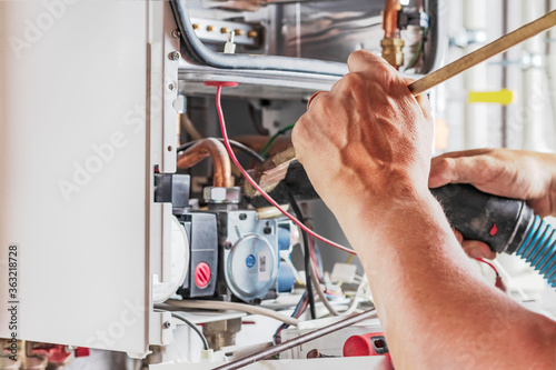 The master sets up a gas boiler, which weighs on the wall. The front dashboard is open. Using a brush and an industrial vacuum cleaner, cleaning from dirt and dirt. photo