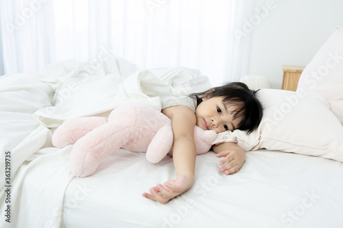 Portrait of a sick little girl sleeping in bed with a pink teddy bear at home