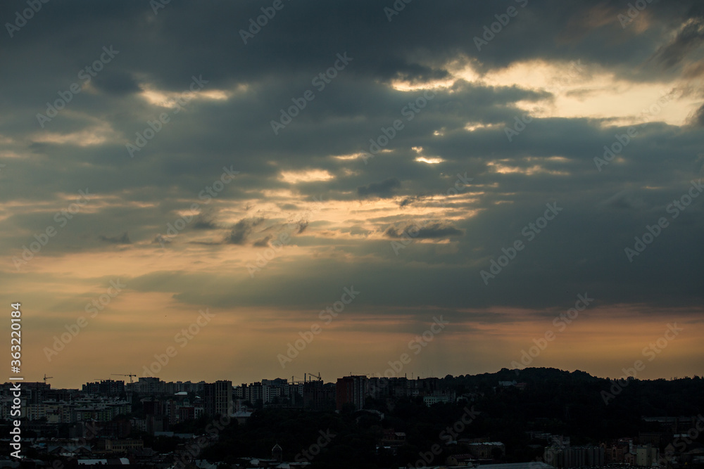 beautiful sunset with grey clouds on dramatic sky above cityscape silhouettes