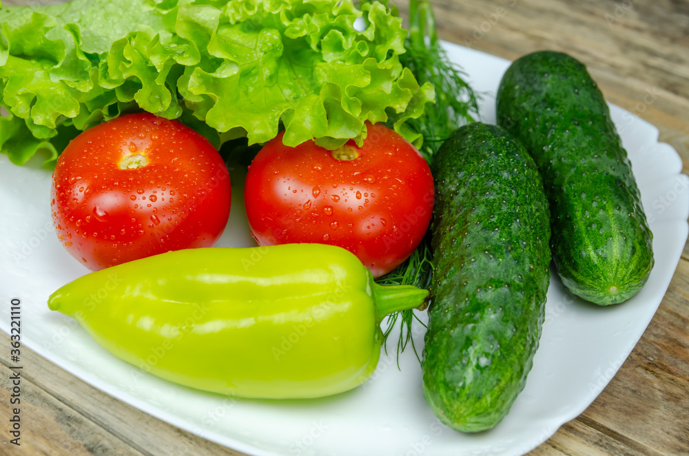 Fresh juicy vegetables peppers, tomatoes, cucumbers lettuce leaves with water drops beautifully laid out on a white plate close-up. Vegetables are in the form of a funny face Fresh juicy vegetables peppers, tomatoes, cucumbers lettuce leaves with water drops beautifully laid out on a white plate close-up. Vegetables are in the form of a funny face