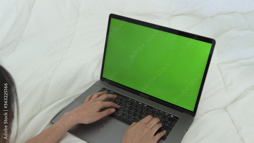 Woman using laptop with looking at green screen on the bed at home. Woman using laptop with looking at green screen on the bed at home.