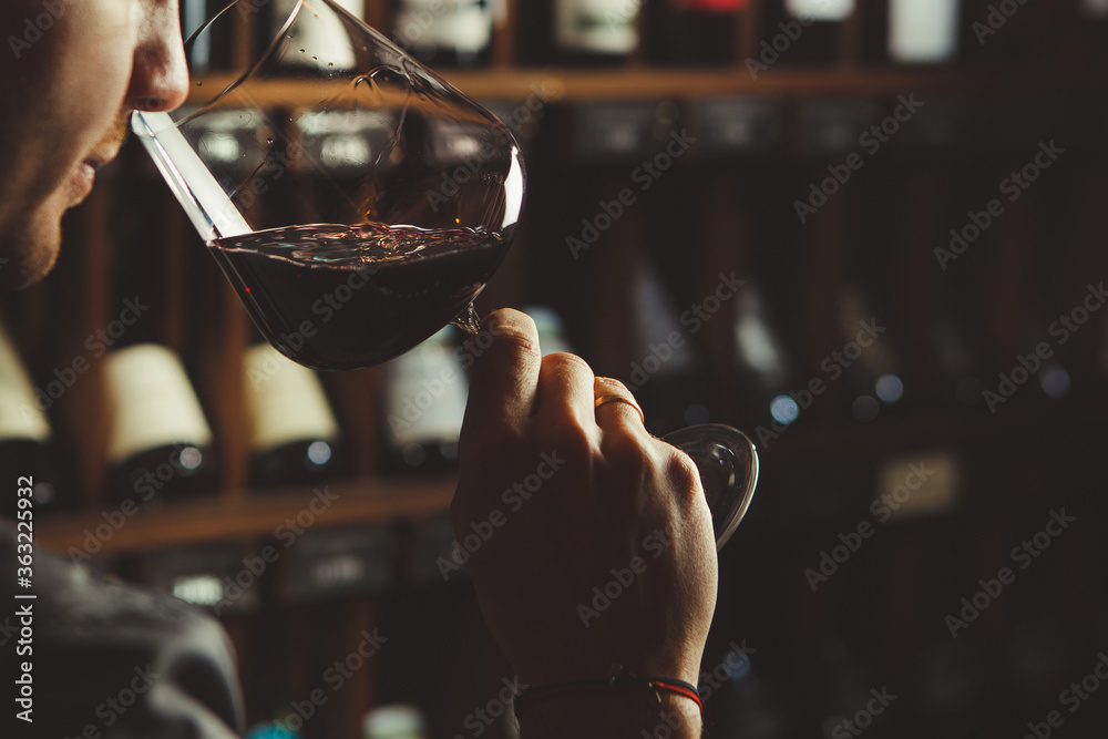 Close-up shot of young sommelier smell red wine on wine cellar background. - obrazy, fototapety, plakaty 