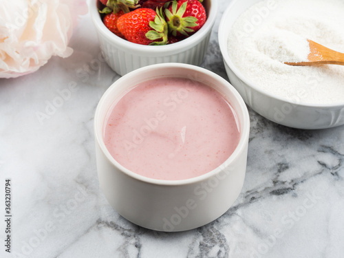 Collagen protein powder in bowl with wooden spoon on marble table. Adding collagen supplement to strawberry yogurt