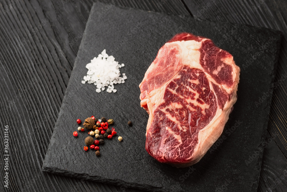 Fresh raw meat with pepper on black slate, on dark background, steak Ribeye