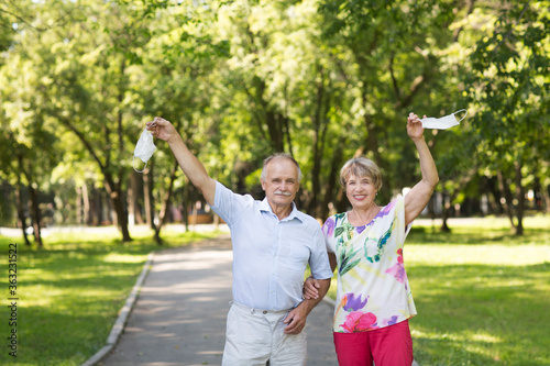 joyful elderly couple hold medical masks with hands up in the summer garden. end of a quarantine 