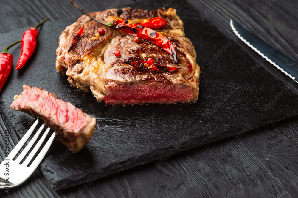 Sliced grilled meat barbecue steak Striploin with knife and fork carving set on black stone slate Sliced grilled meat barbecue steak Striploin with knife and fork carving set on black stone slate