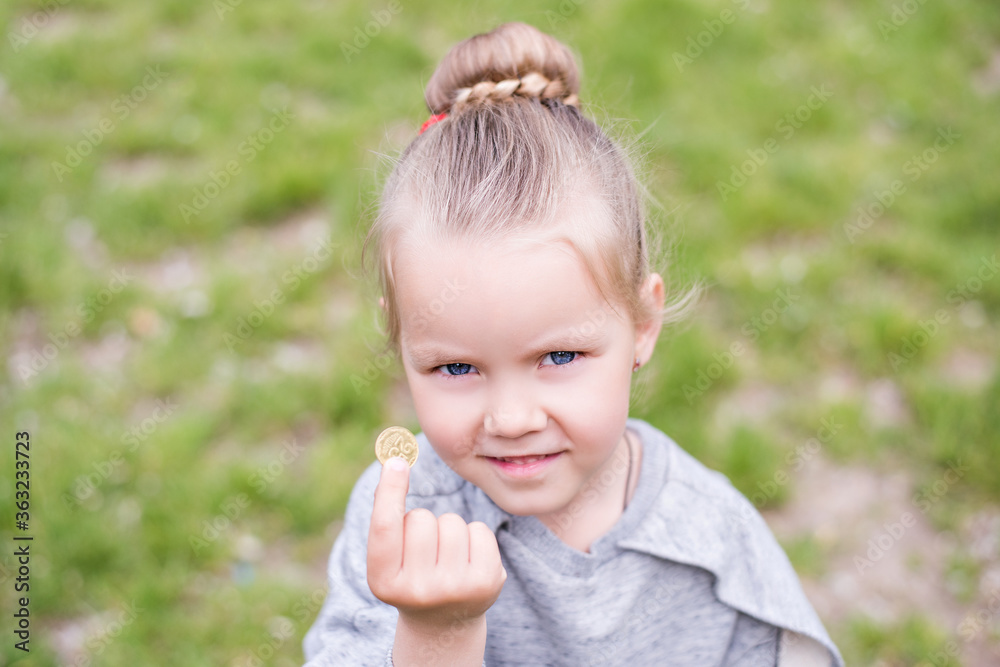 Little blond girl with blue eyes, hair arranged in a bun, wearing a gray dress, close-up portrait, looking into the camera, smiling, bored, playing on a lawn, sitting on the machine tires. Preschool Little blond girl with blue eyes, hair arranged in a bun, wearing a gray dress, close-up portrait, looking into the camera, smiling, bored, playing on a lawn, sitting on the machine tires. Preschool