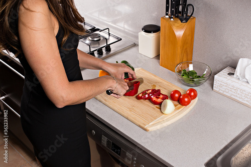 Wooden cutting board with vegetables and a knife, a woman cuts vegetables for salad. Woman in black dress, cooking on a black table. different views.
