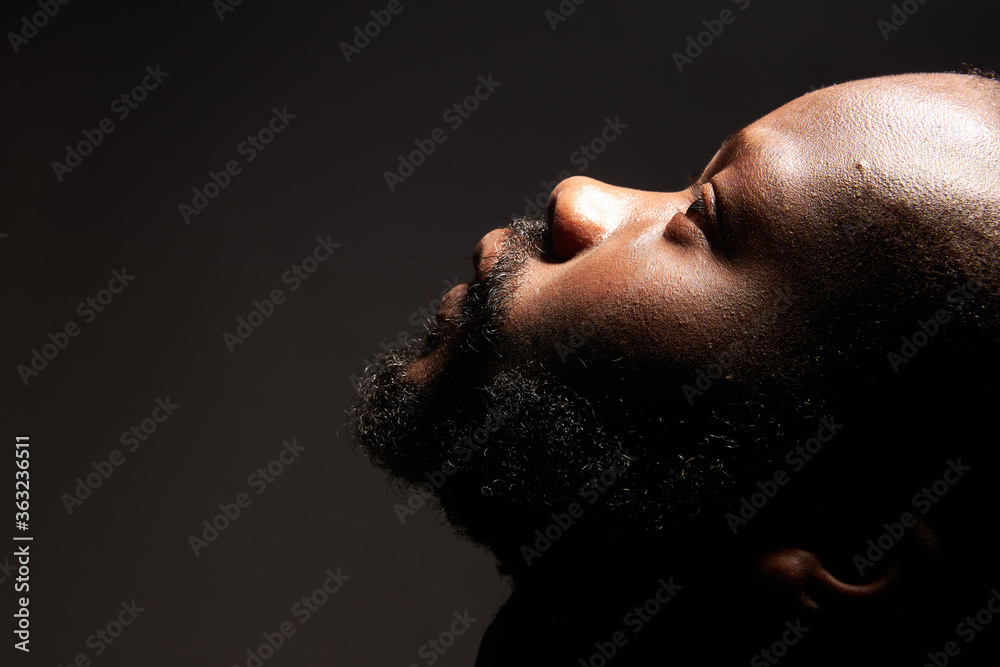 portrait of a dark-skinned handsome guy with a beard looking uphill on a black background