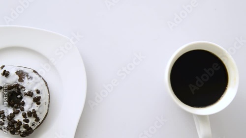 Breakfast at the office, a donut and a cup of coffee on a white table. Overhead scene.