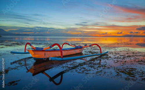 Seascape. Fisherman boat jukung. Traditional fishing boat at the beach during sunrise. Colorful sky. Amazing water reflection. Sanur beach, Bali