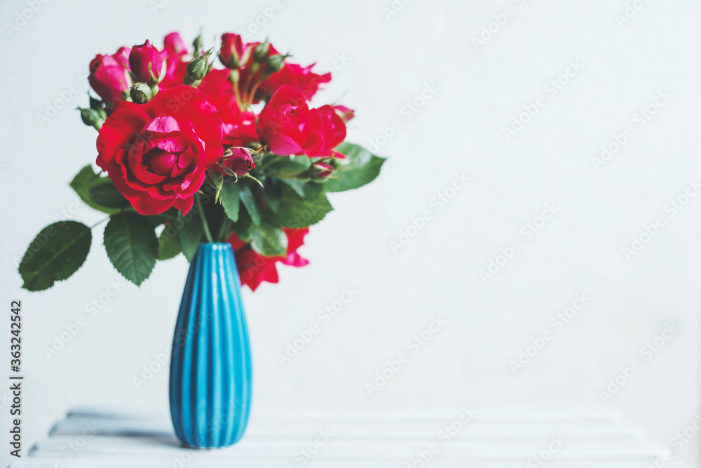 Fototapeta premium Bouquet of red roses in a blue vase on a white background, Place for text.