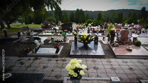 Graves with many flowers in the cemetery Hungary/Europe. Marble tombstone granite monument headstone, artificial flowers. 4k