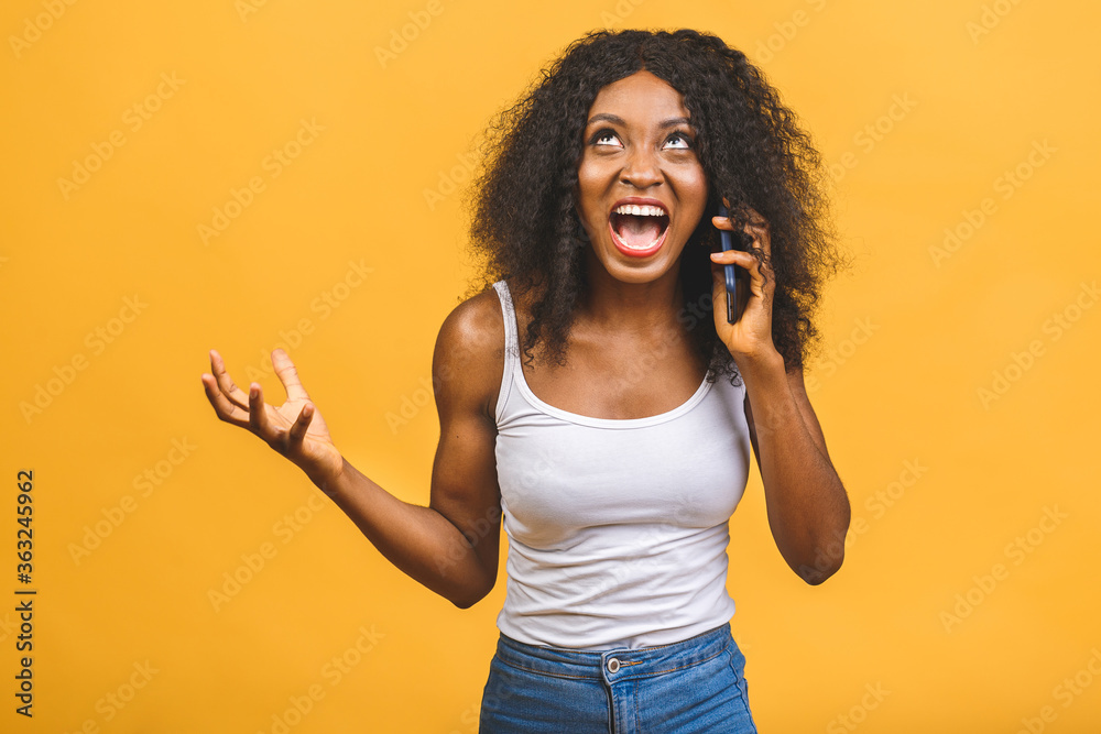 Angry mixed race black african american woman shouting in mobile phone, isolated over yellow background. Angry mixed race black african american woman shouting in mobile phone, isolated over yellow background.