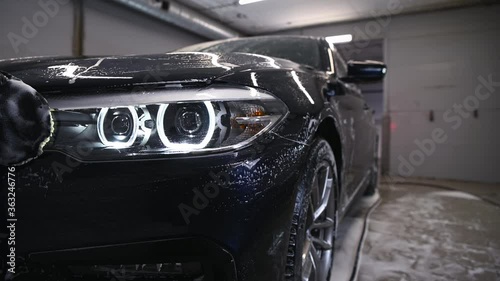 Car detailing - the man washes headlights of a car with a hand covered with a special wash glove, close-up.