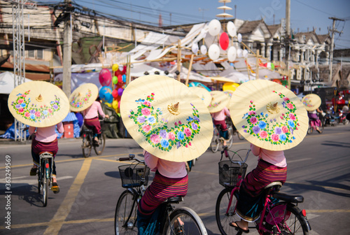 Group of women in traditional costume hold umbrella and ride bicycle parade show in 33th anniversary Bosang umbrella festival,San Kampaeng, Chiang Mai, Thailand. photo